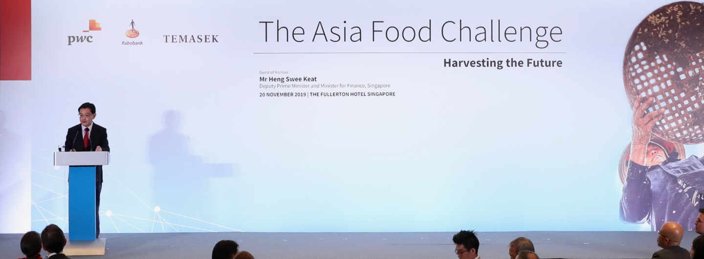 Man at podium, "Asia Food Challenge," PwC, Rabobank, and Temasek logos on a backdrop with a rice harvester image.